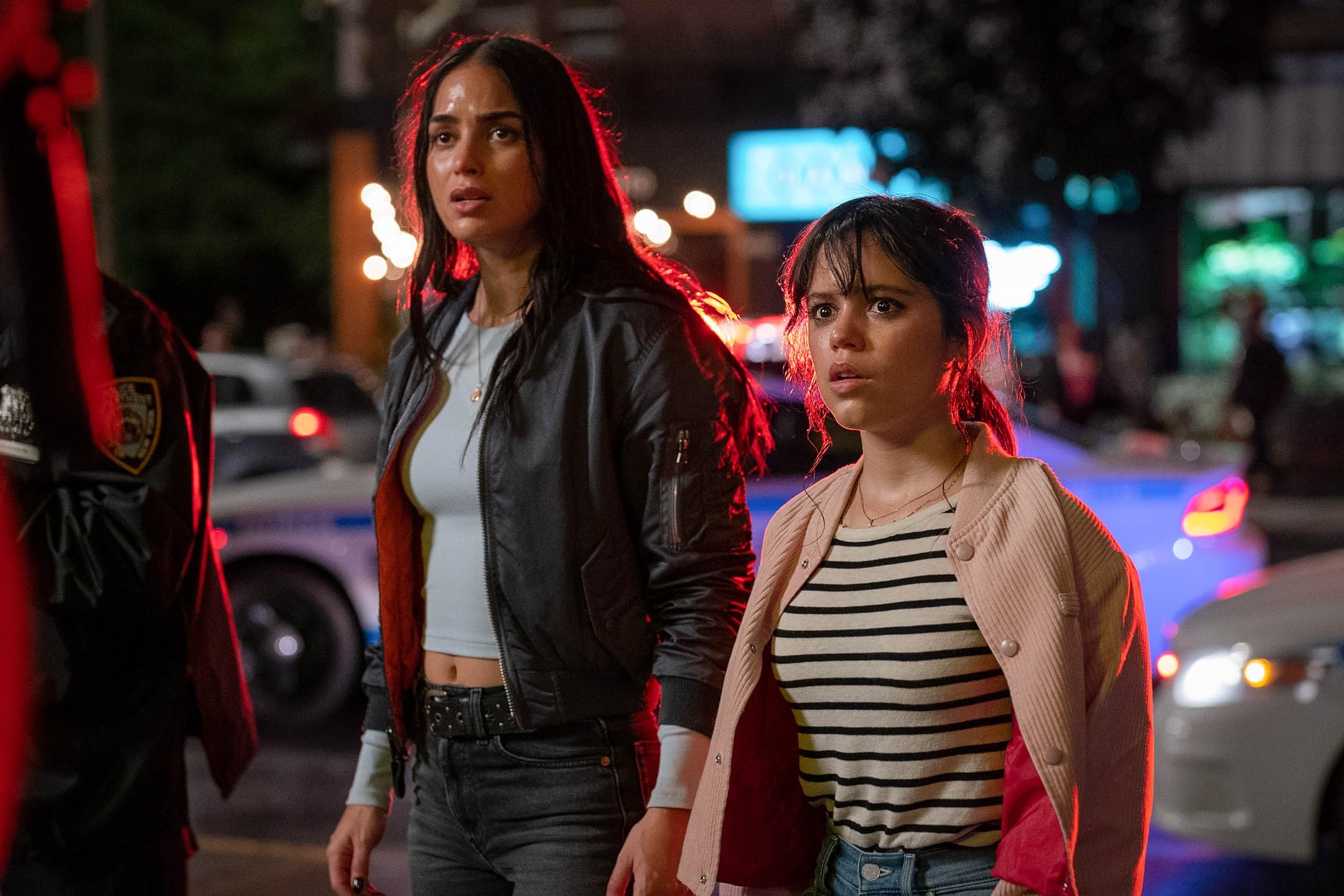 Melissa Barrera and Jenna Ortega stand beside police cars during a scene on a New York street in Scream 6.